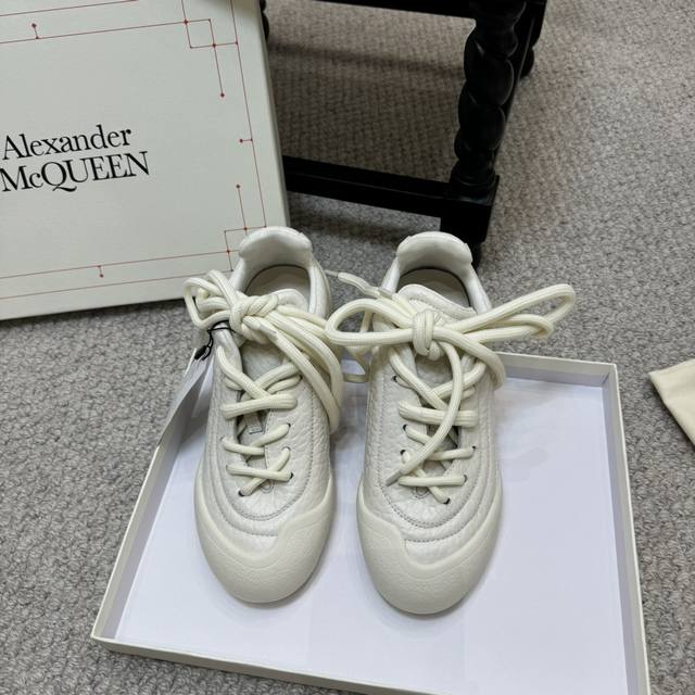 White low-top sneakers feature grained leather with varying lace sizes, a shaped